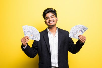 successful-indian-entrepreneur-with-dollar-banknotes-hand-classical-suit-looking-camera-with-toothy-smile-while-standing-against-yellow-wall_231208-2660.jpg